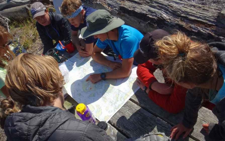 a group of outward bound students examine a map on a sea kayaking expedition 
